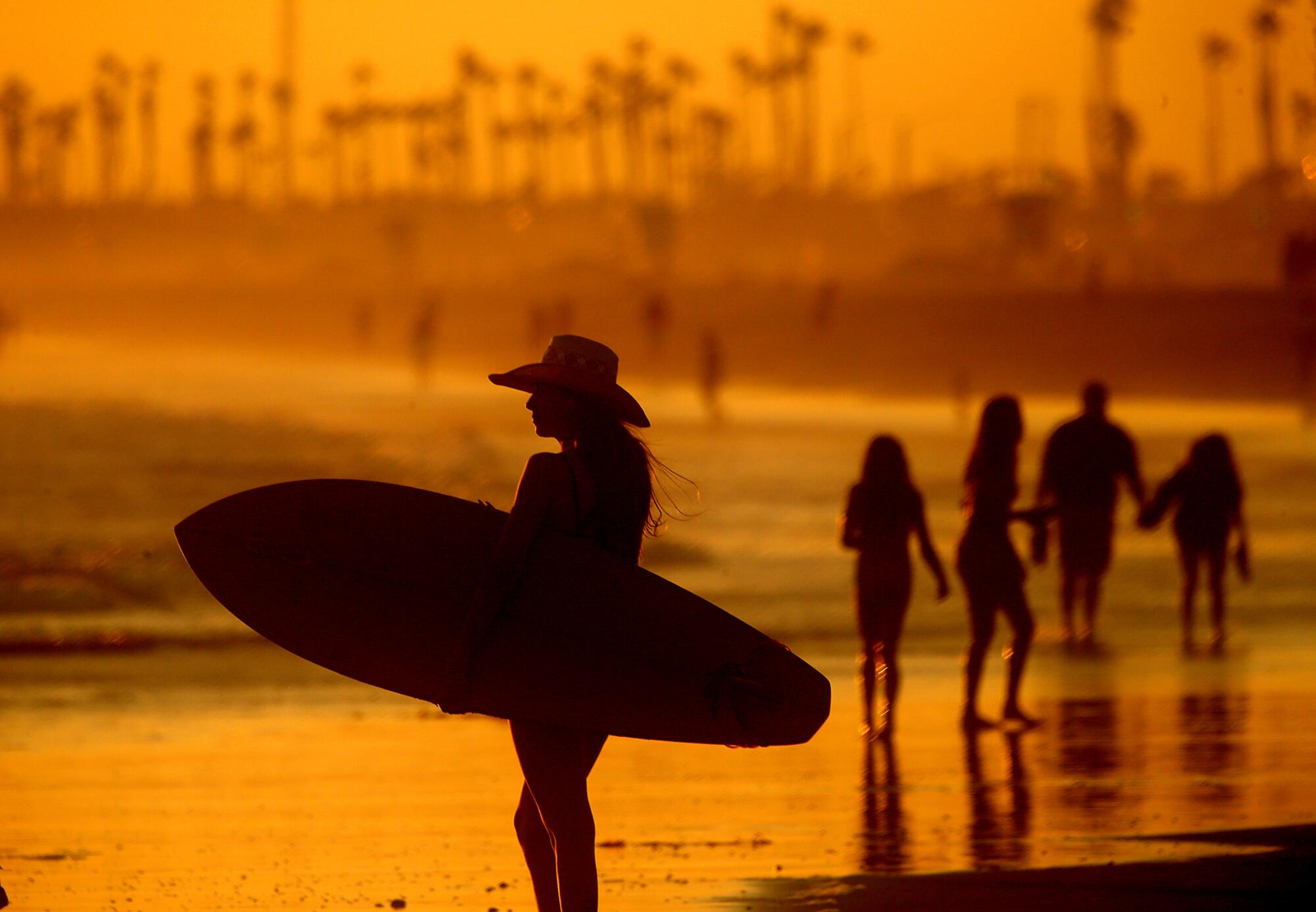 Les amateurs de plage profitent de la brume rafraîchissante de l'océan alors que le soleil se couche sur Huntington Beach. 
