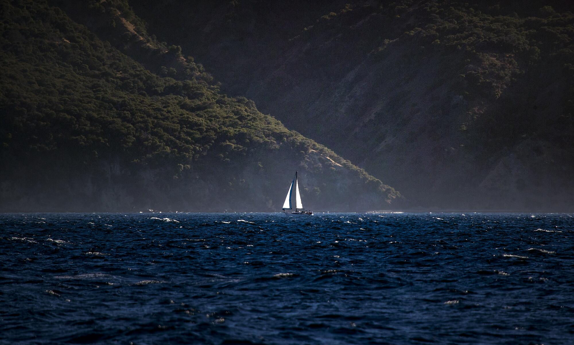 Les montagnes d’une île s’élèvent derrière un voilier solitaire.