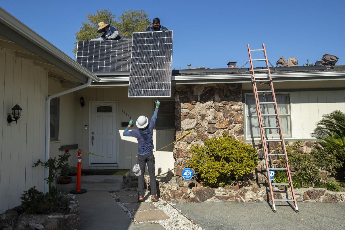 Des ouvriers installent des panneaux solaires sur le toit d'une maison.
