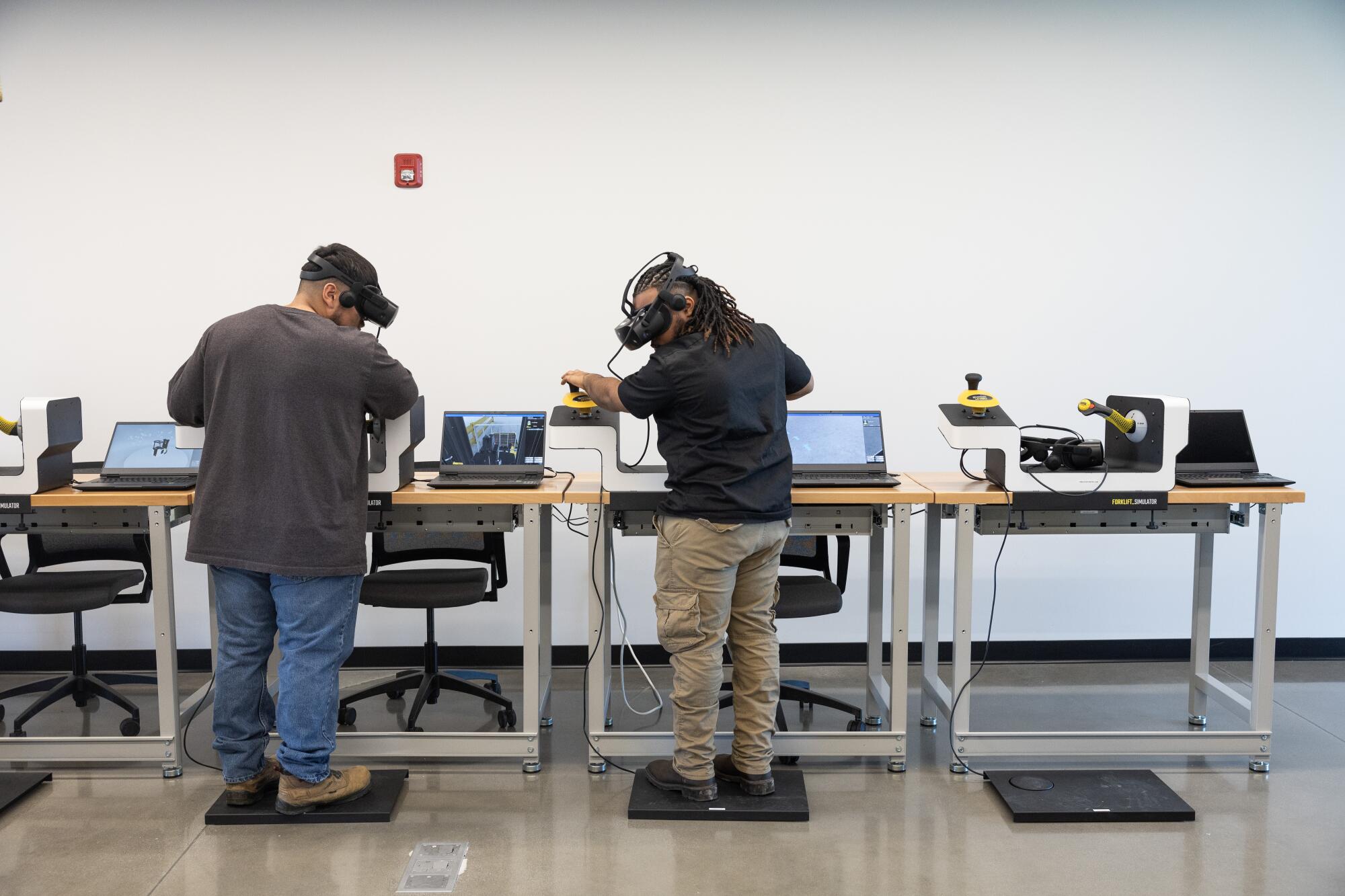 Deux hommes portent des casques VR qui simulent les opérations d'un chariot élévateur.  