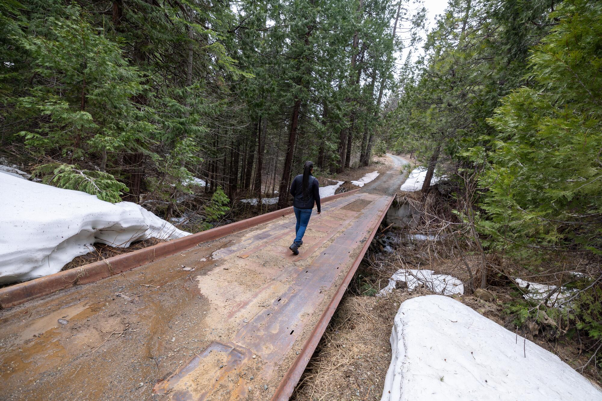 Une femme traverse un pont sur un chemin forestier.