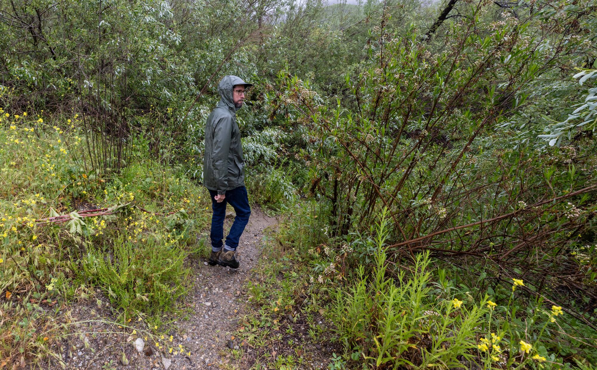 Un homme vêtu d’une veste imperméable à capuche fait de la randonnée le long d’un sentier détrempé. 
