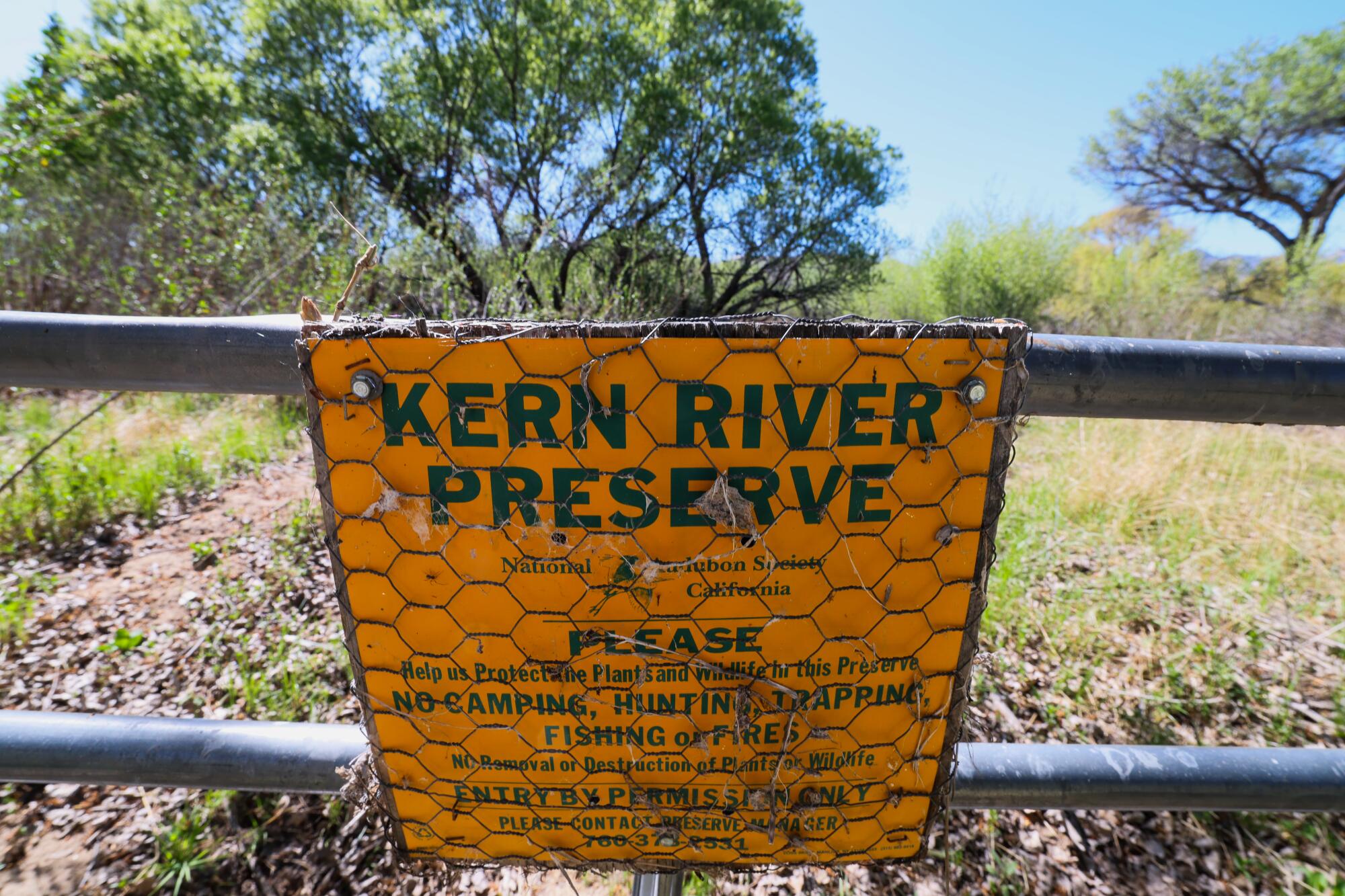 Un panneau indique « Kern River Preserve » sur une porte, avec des arbres en arrière-plan.