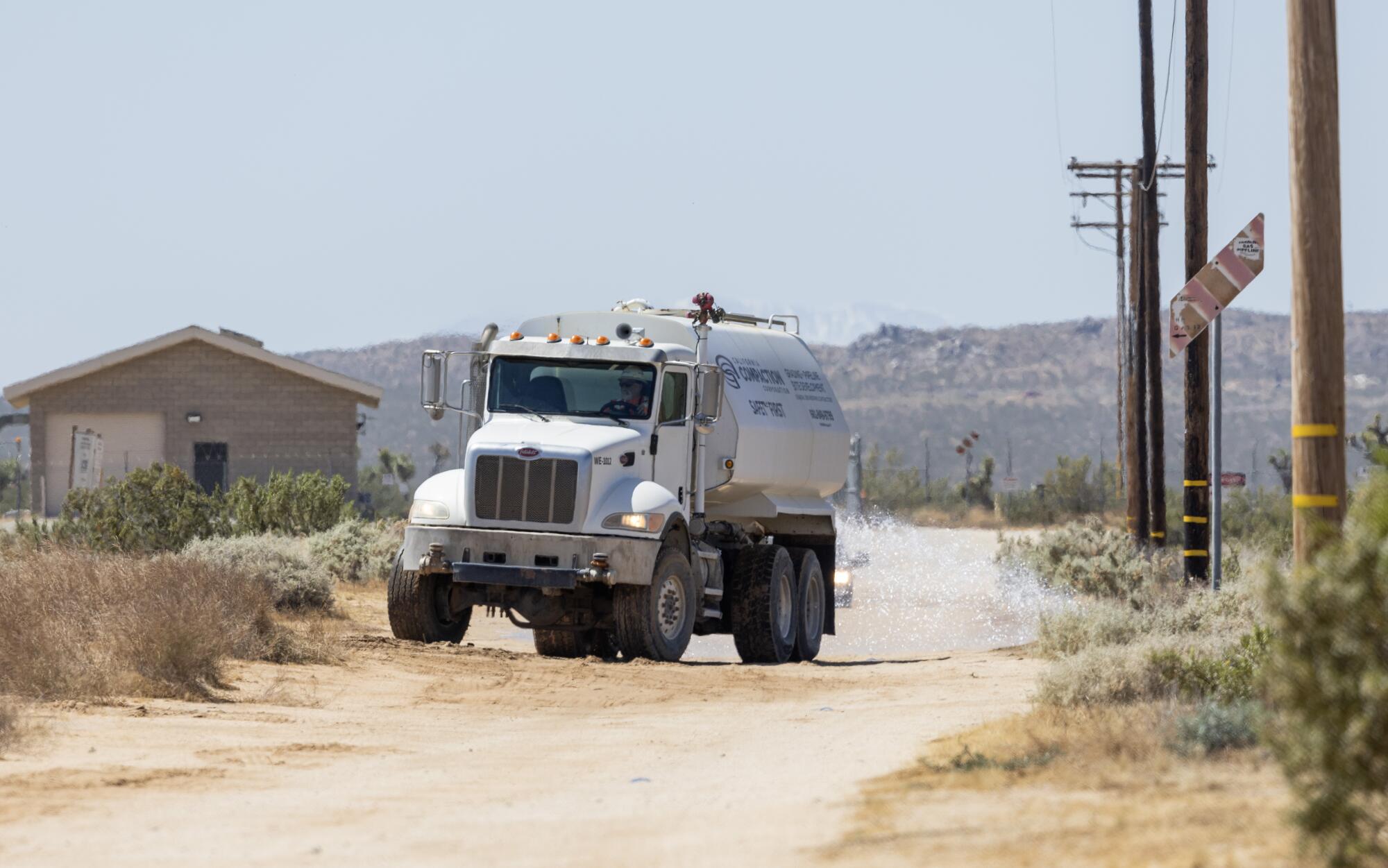 Un camion-citerne répand de l’eau sur un chemin de terre dans le désert.