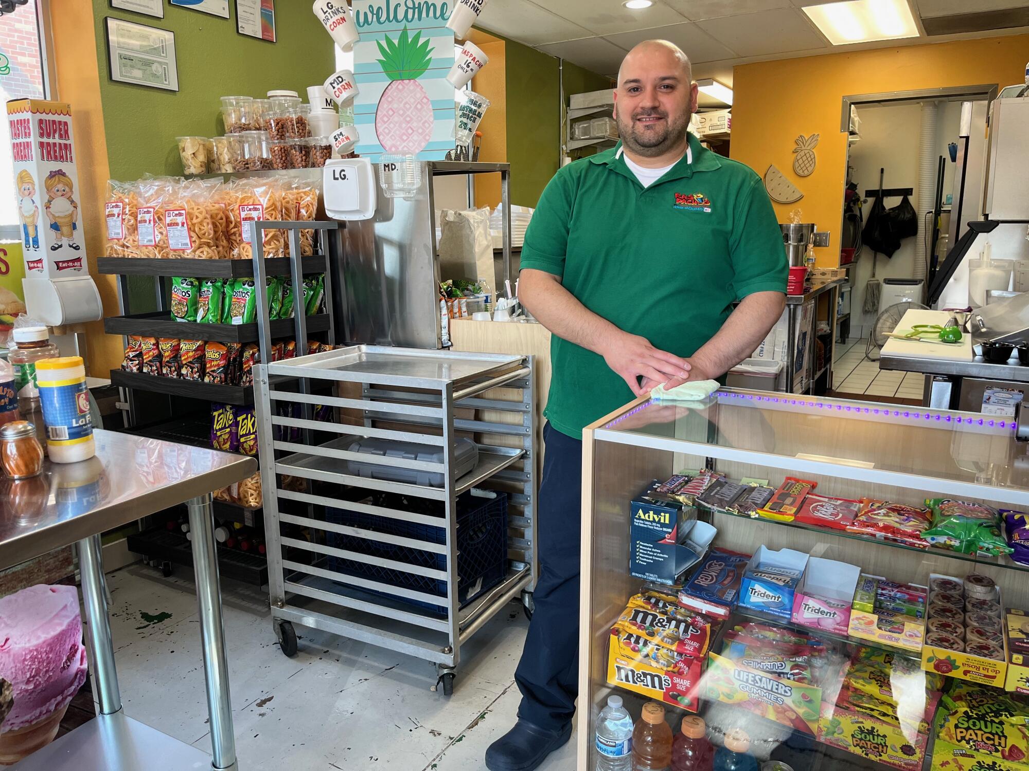 Un homme en chemise verte se tient dans un magasin avec des bonbons et des collations.