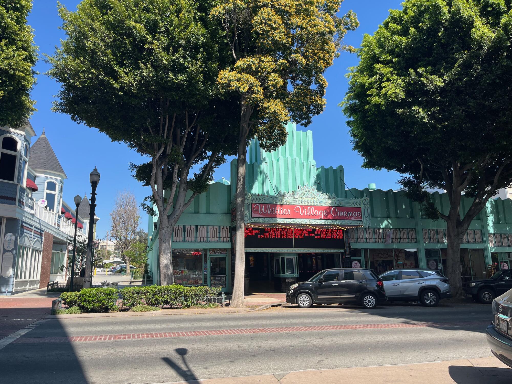De grands arbres flanquent l'entrée d'une salle de cinéma art déco, le Whittier Village Cinema