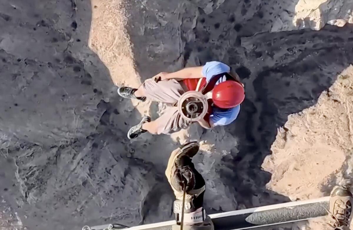 Vue d'en haut d'une personne portant un casque rouge hissée vers un hélicoptère.