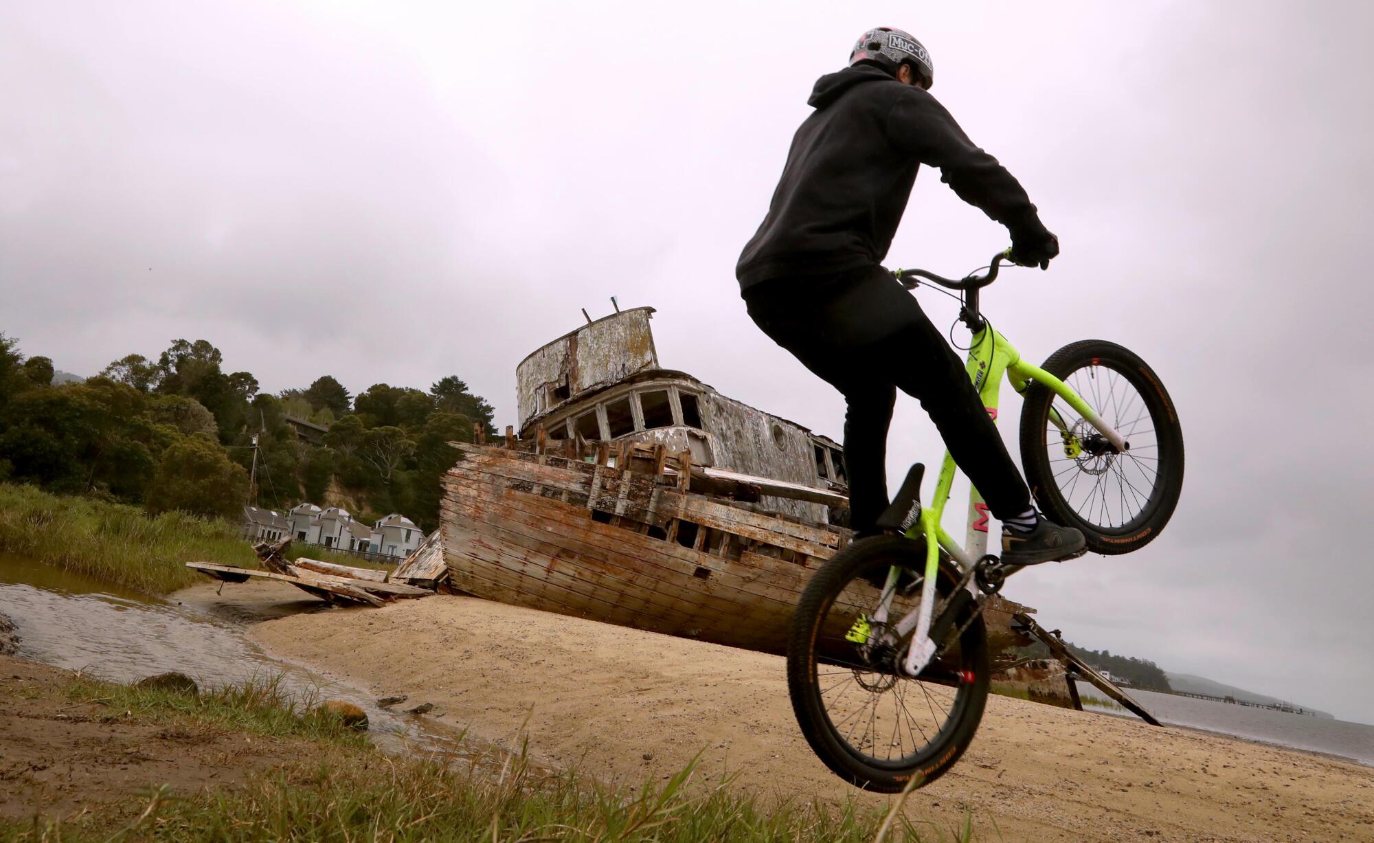 Un jeune homme sur un vélo jaune saute au-dessus d’une crique près d’un bateau d’inscription.
