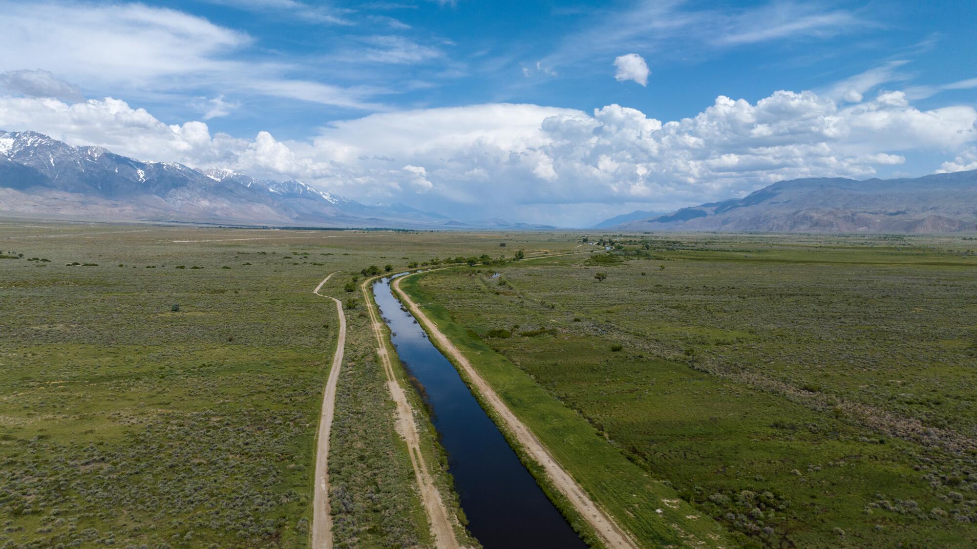 Une vue aérienne de l'aqueduc de Los Angeles traversant des espaces verts sous un ciel avec des nuages ​​blancs.