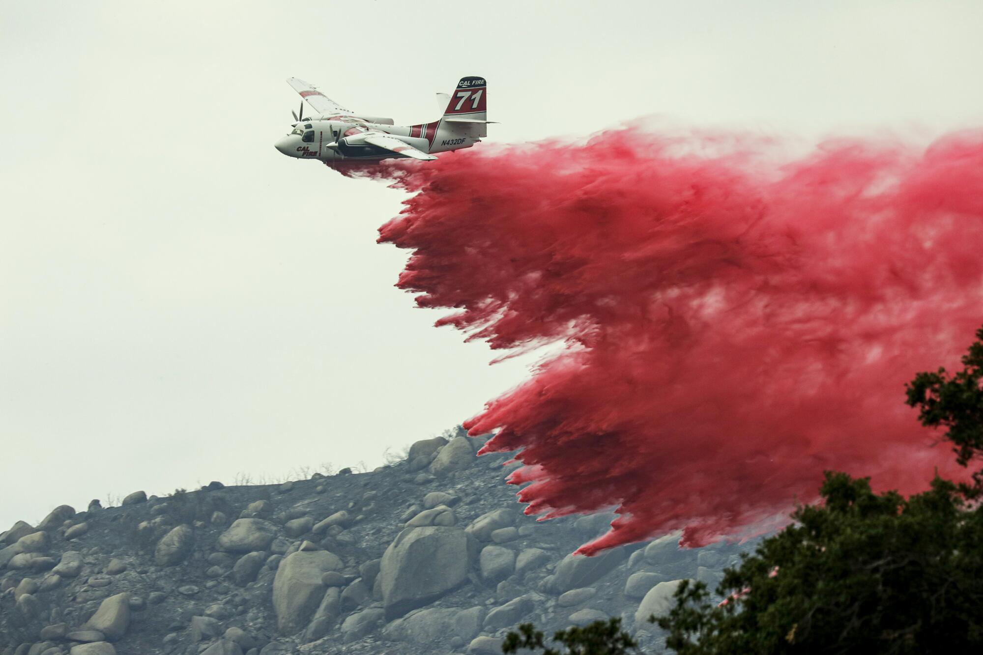 Un avion largue un produit ignifuge sur un feu de broussailles qui fait rage sur une colline rocheuse.  