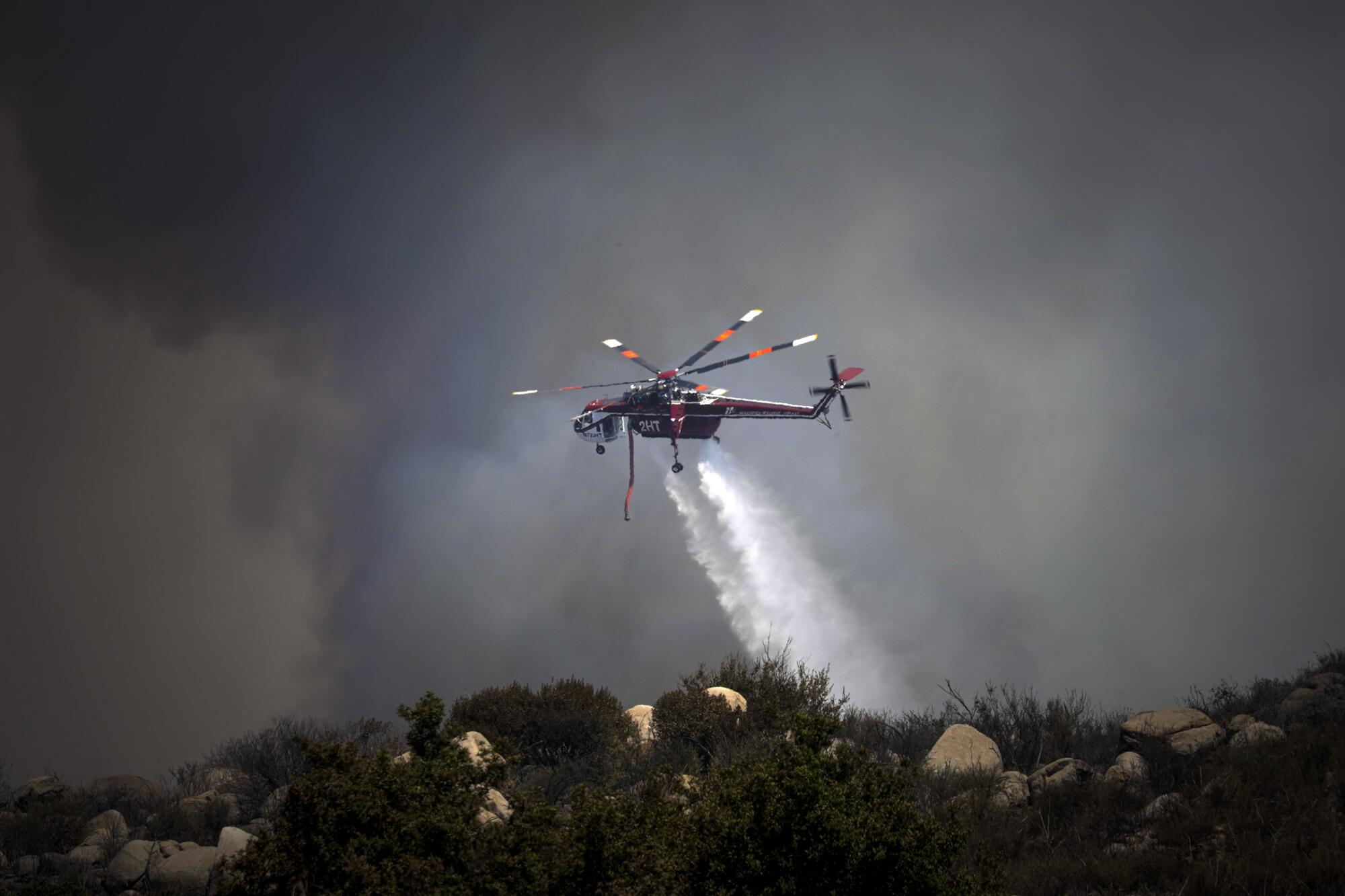 Un hélicoptère largue de l'eau sur une colline en feu. 