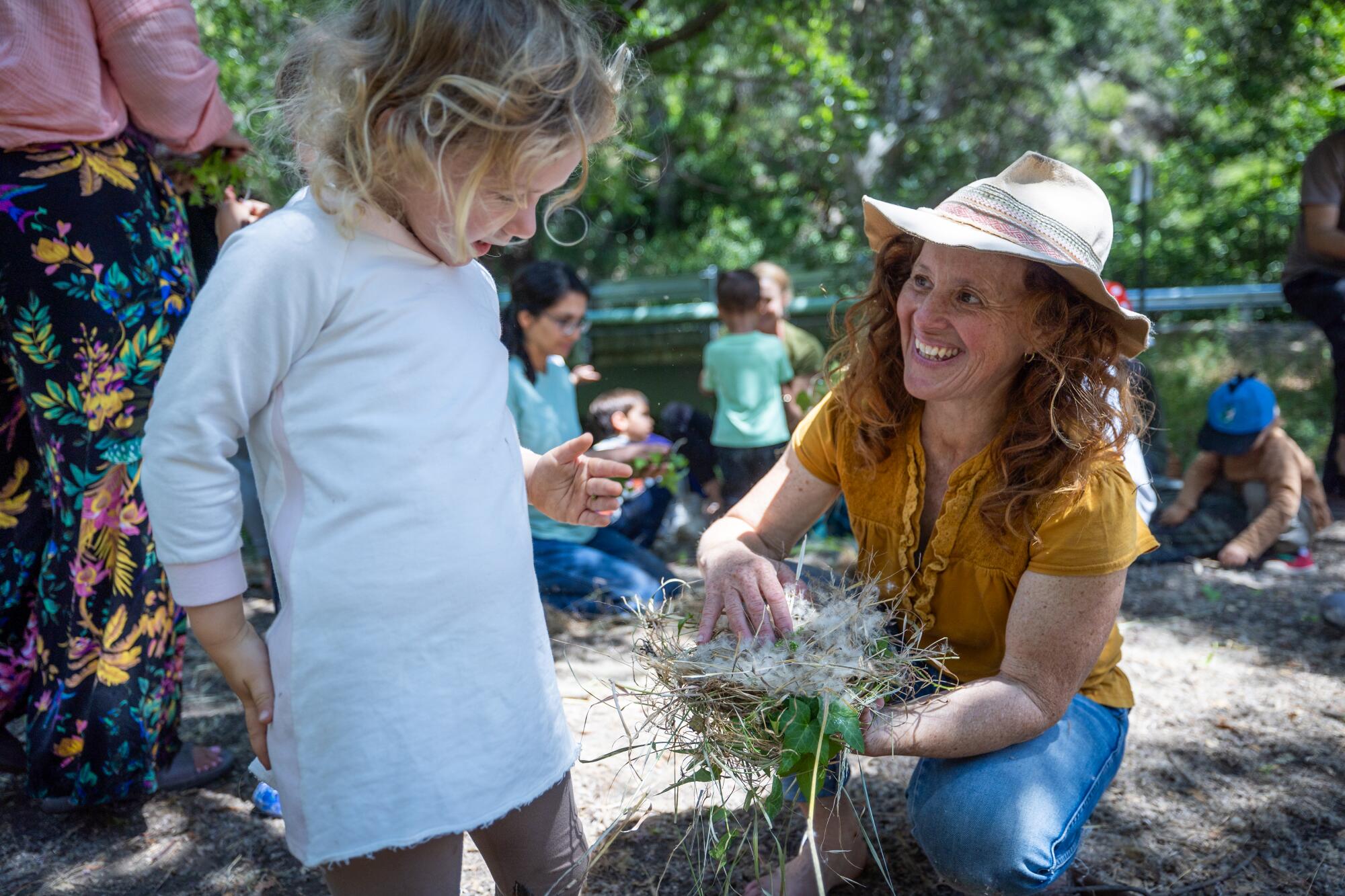 Une femme montre à un enfant une poignée de brindilles et d’herbe.