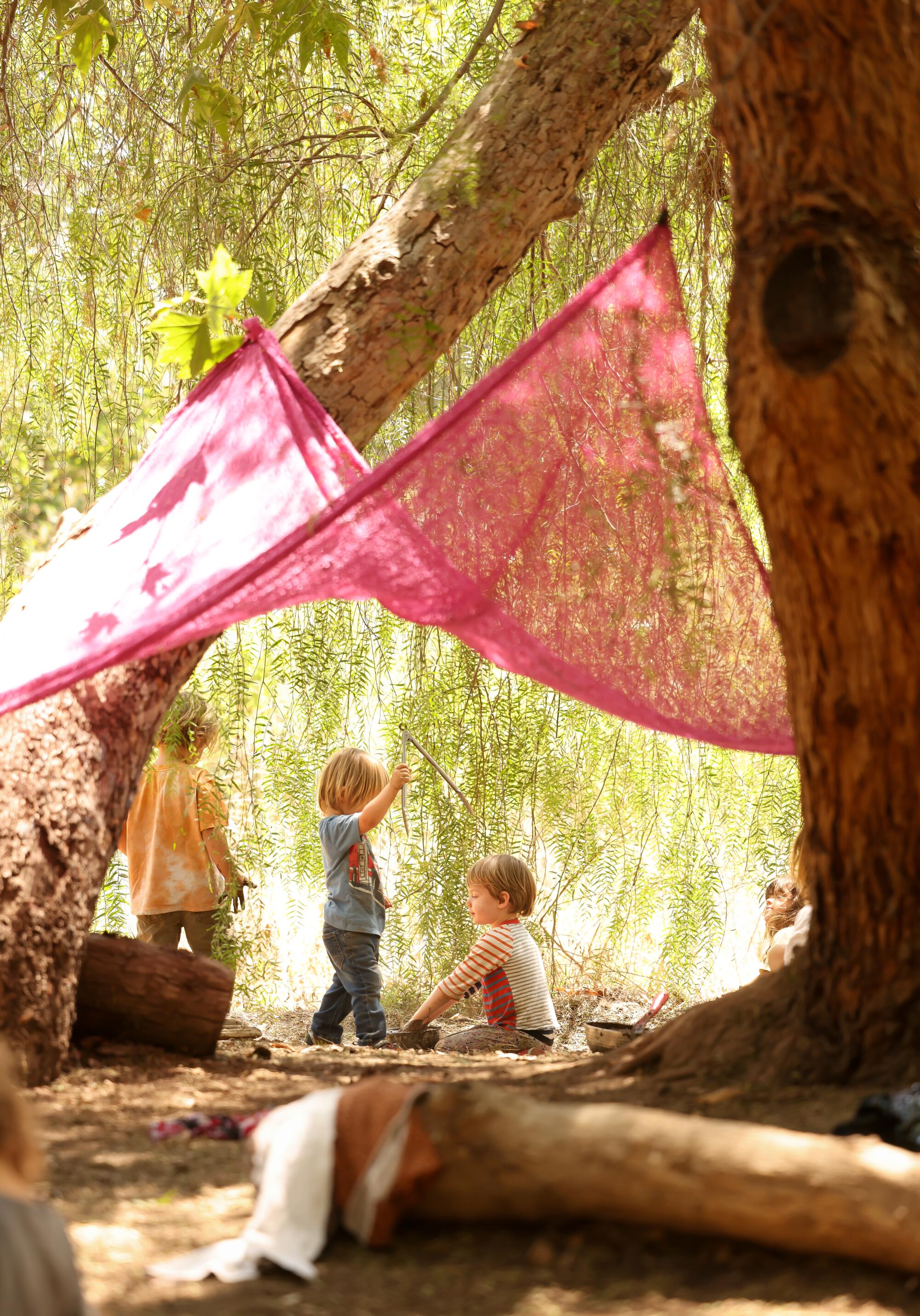 Les enfants jouent sous une toile d’ombrage tendue entre les arbres.