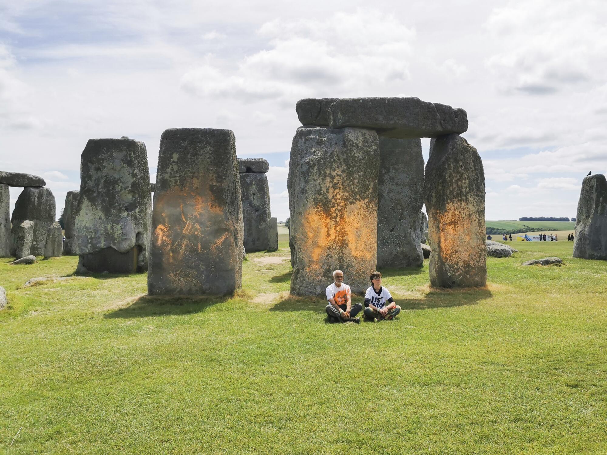 Des manifestants sont assis devant un Stonehenge peint à la bombe.