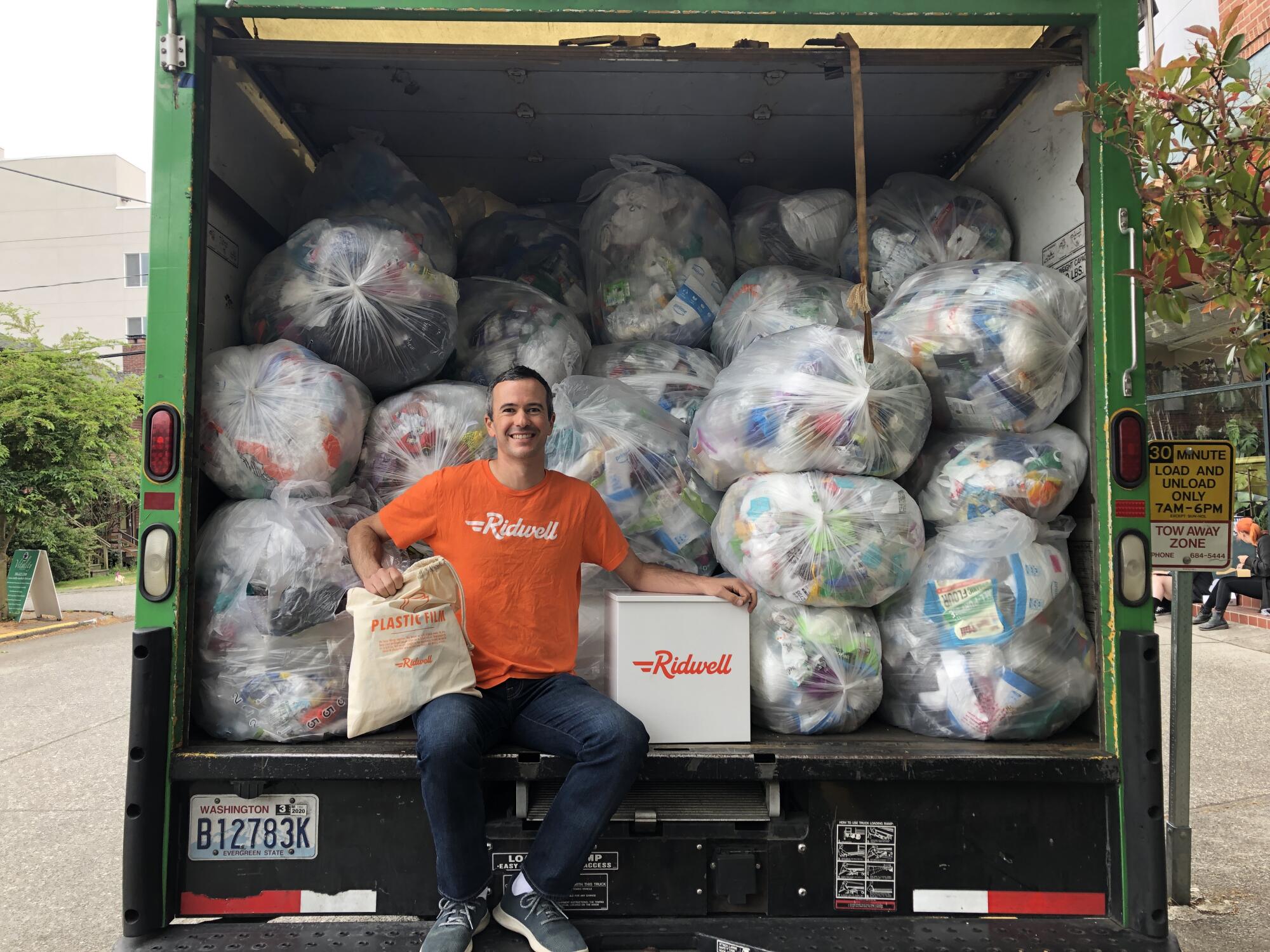 Ryan Metzger, de Ridwell, est assis à l'arrière d'un camion porte-conteneurs chargé de sacs en plastique remplis de déchets.