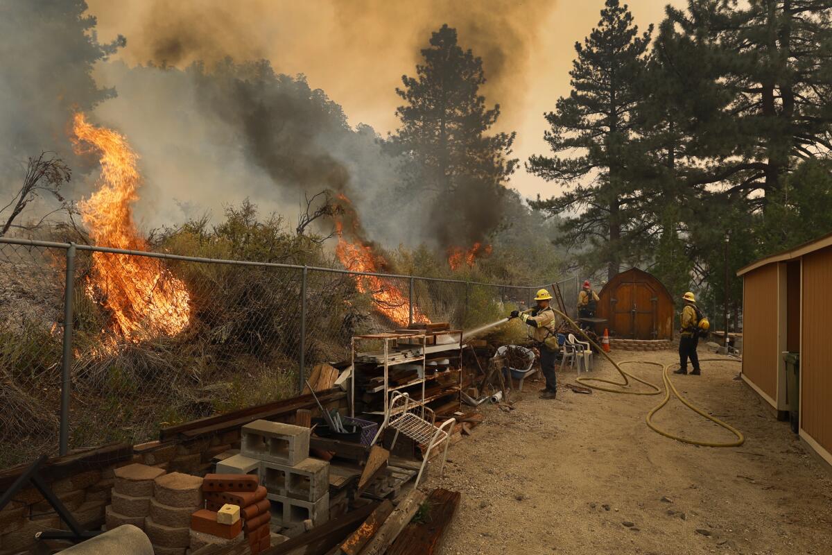 Les pompiers pulvérisent de l'eau alors que les flammes s'approchent d'une propriété.