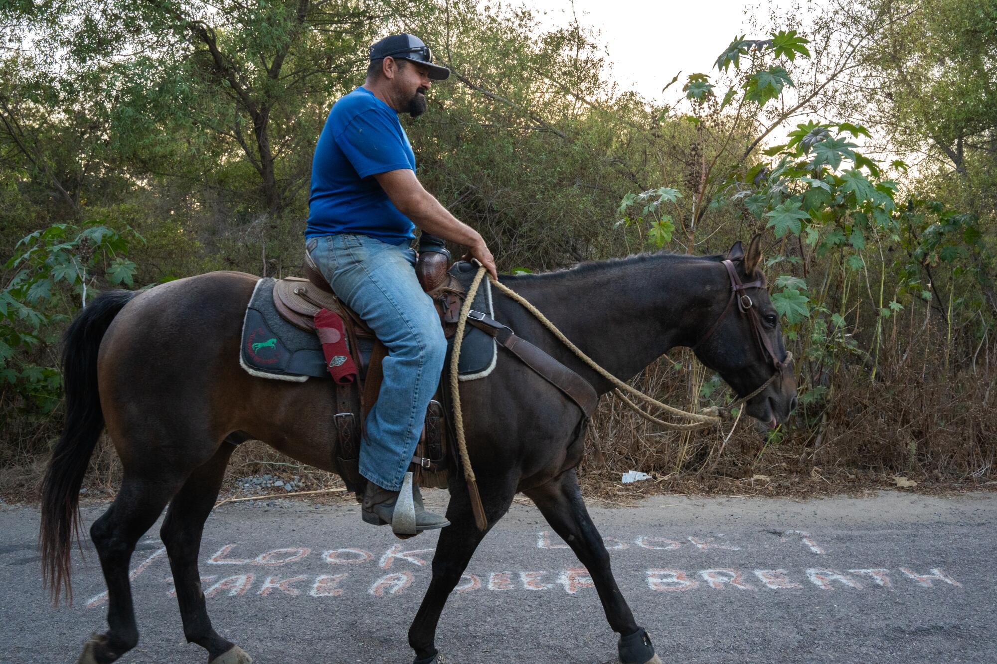 Un cavalier promène son cheval sur le trottoir traversant la rivière Tijuana. Sur l'asphalte on peut lire : "Regarde, respire profondément." 