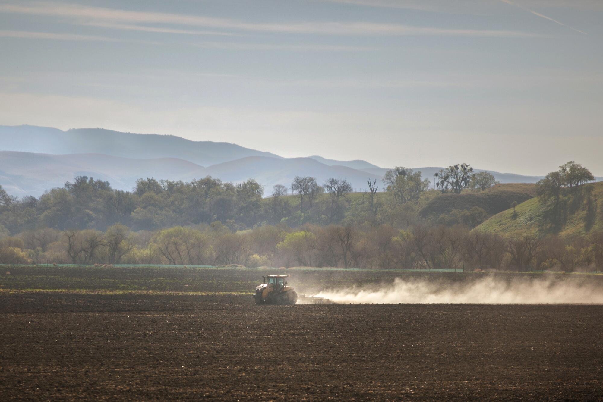 Un tracteur laboure un champ alors qu'une traînée de poussière s'élève derrière lui.