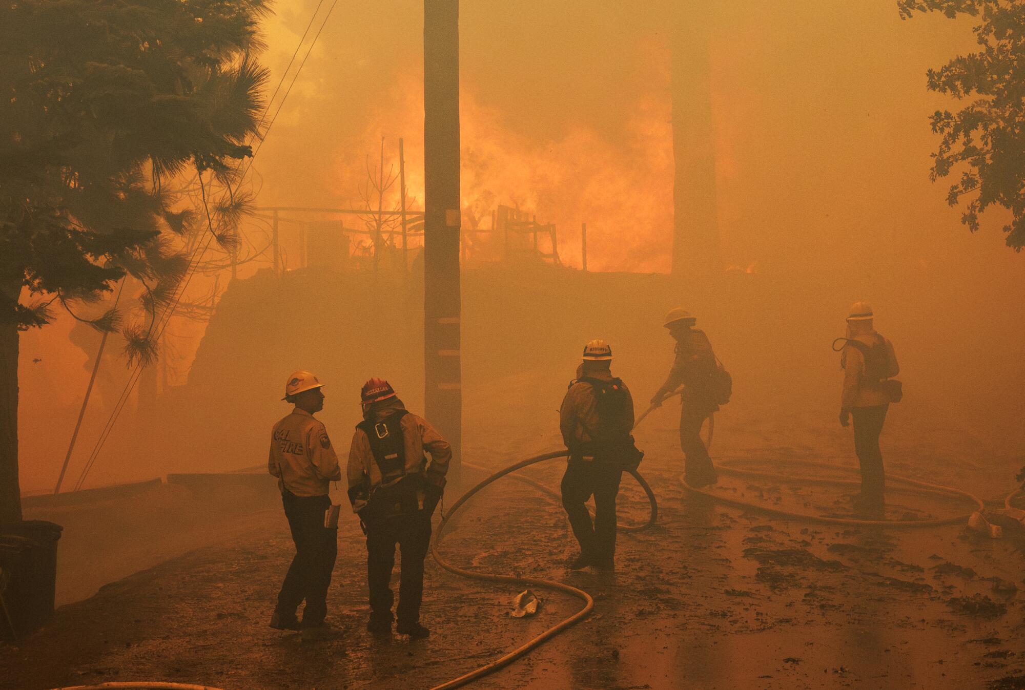 Les équipes de pompiers, au premier plan, se tiennent au milieu d'une brume orange tandis que les flammes font rage en arrière-plan