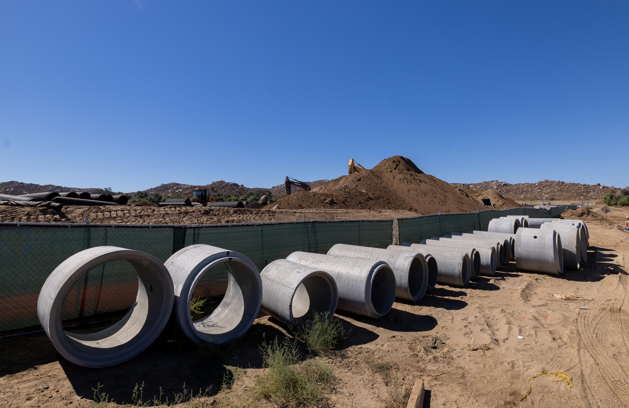 Des sections de tuyaux en béton sont placées côte à côte sur un chantier de construction. 
