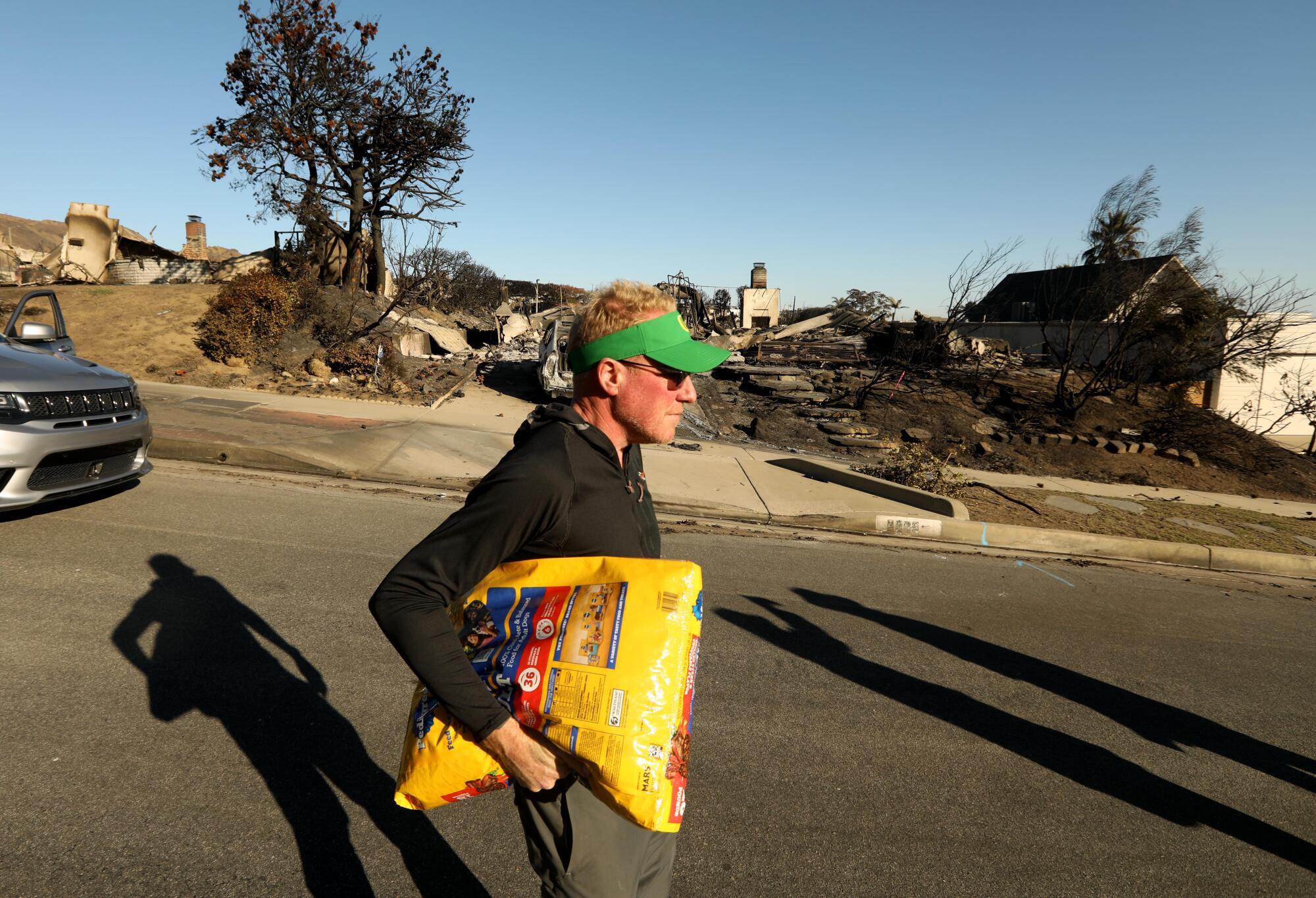 Un homme porte un sac de nourriture pour chien sous son bras alors qu'il passe devant des maisons détruites par un incendie.