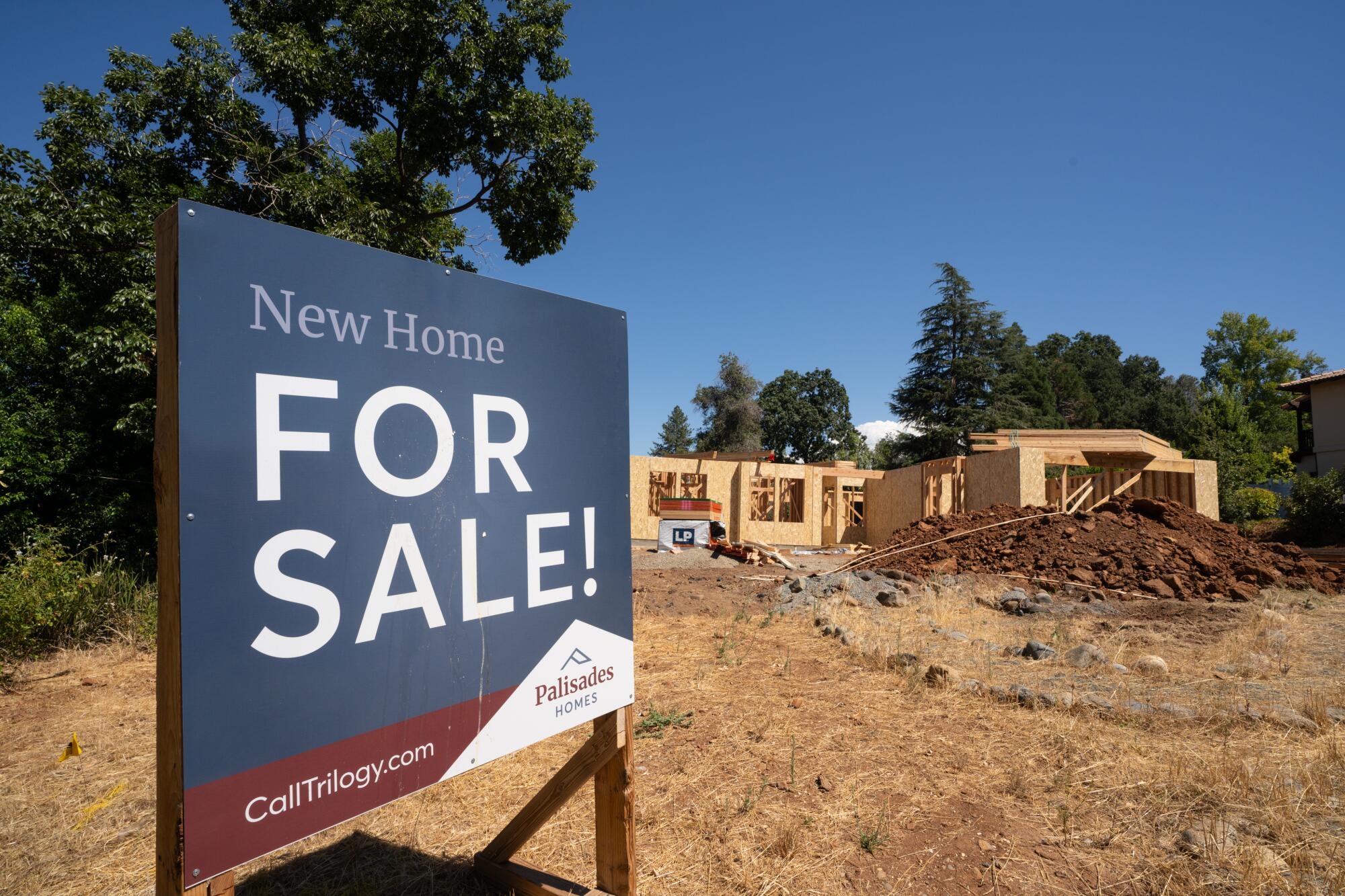 Un panneau à vendre au premier plan et une maison nouvellement construite en arrière-plan près des arbres.