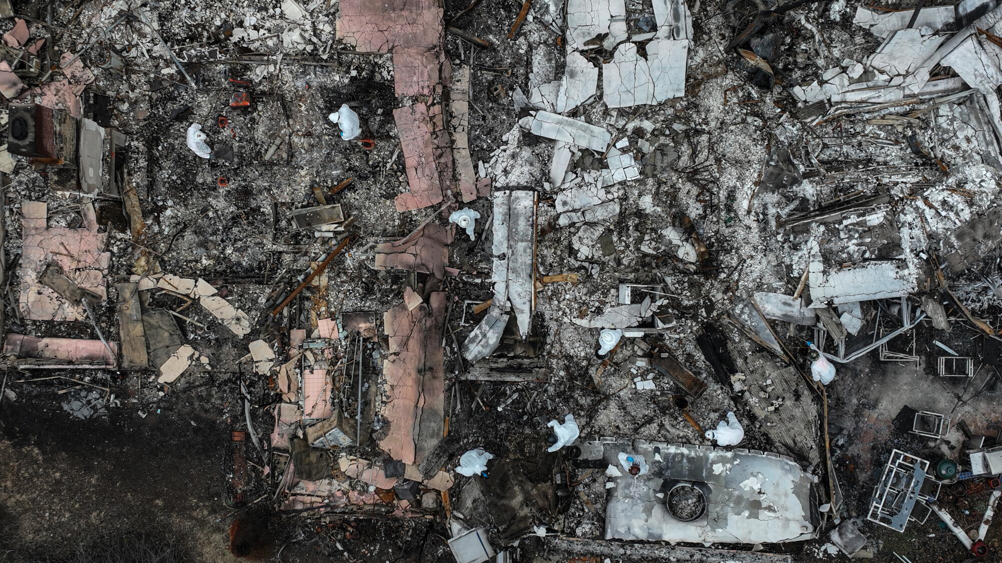Les équipages de l'EPA en combinaison de dangers blancs peignent les ruines des maisons brûlées dans le feu des Palisades en vue aérienne.