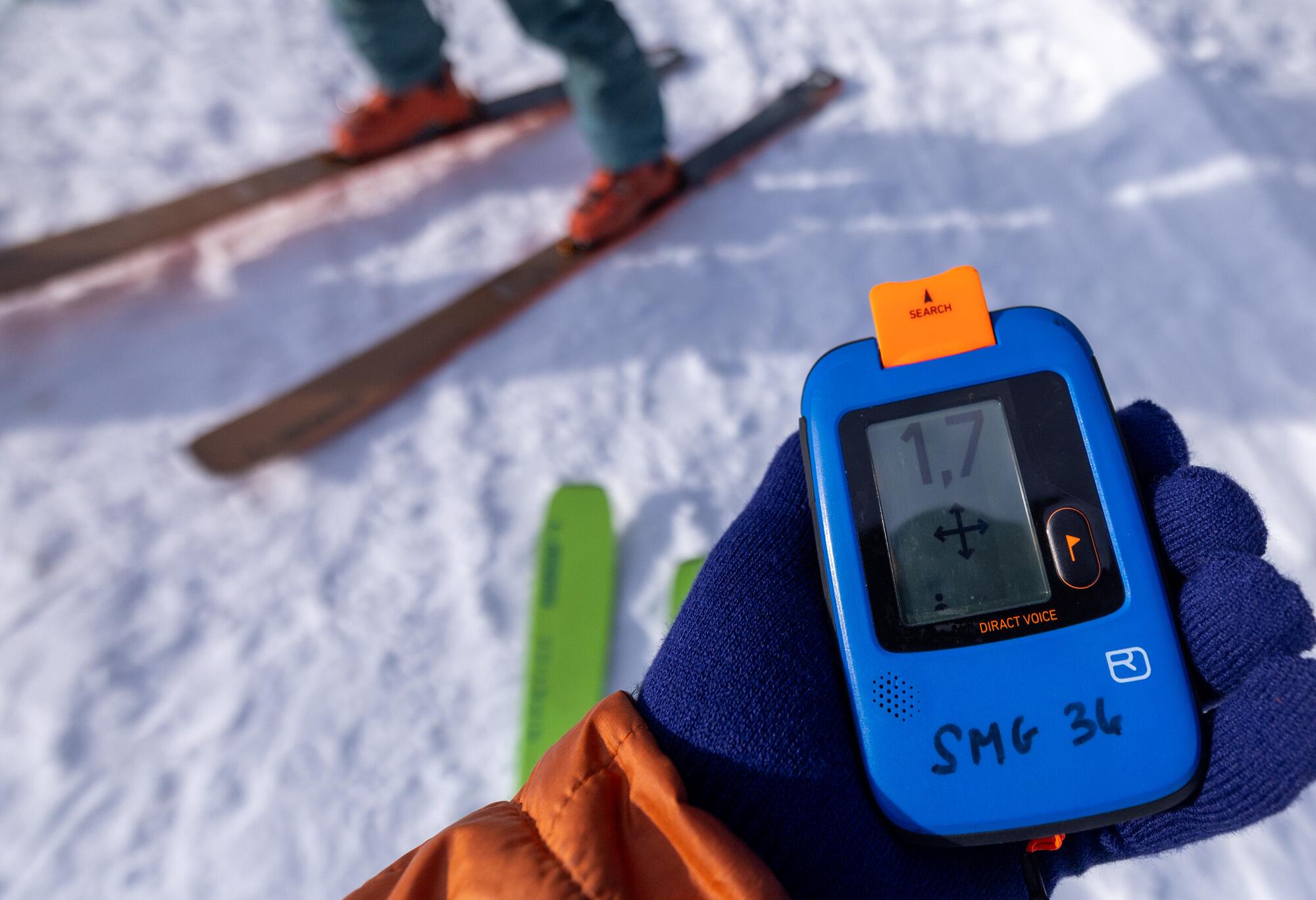 Un skieur tient une balise de sauvetage d'avalanche dans une main à mitaine.