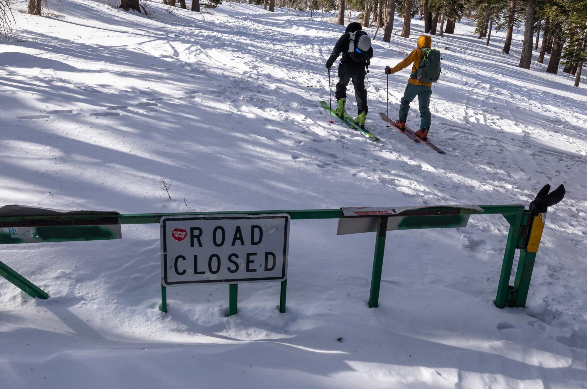 Deux skieurs passent un panneau "Route fermé" sur leur randonnée sur une pente de l'arrière-pays. 