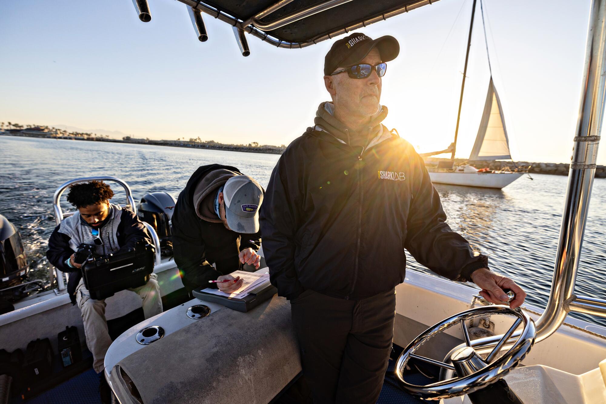 Un homme pilote le bateau alors que son équipe cherche de grands requins blancs au large de Huntington Beach