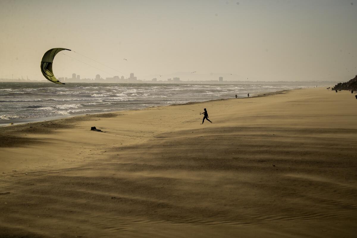 Un surfeur de cerf-volant se dirige sur du sable soufflant sur la plage pour surfer au milieu de vents forts et rafales à Huntington Beach.