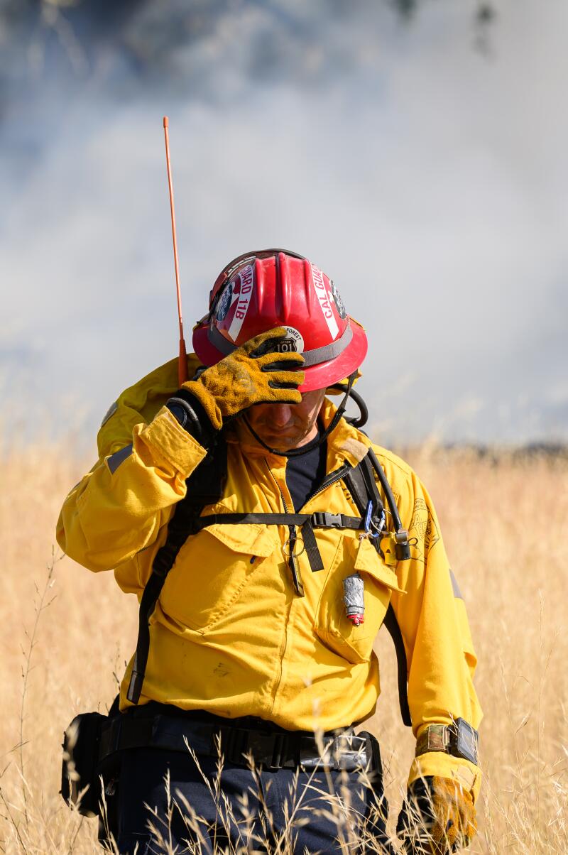   Un pompier dans un casque rouge marche dans un champ fumé.  