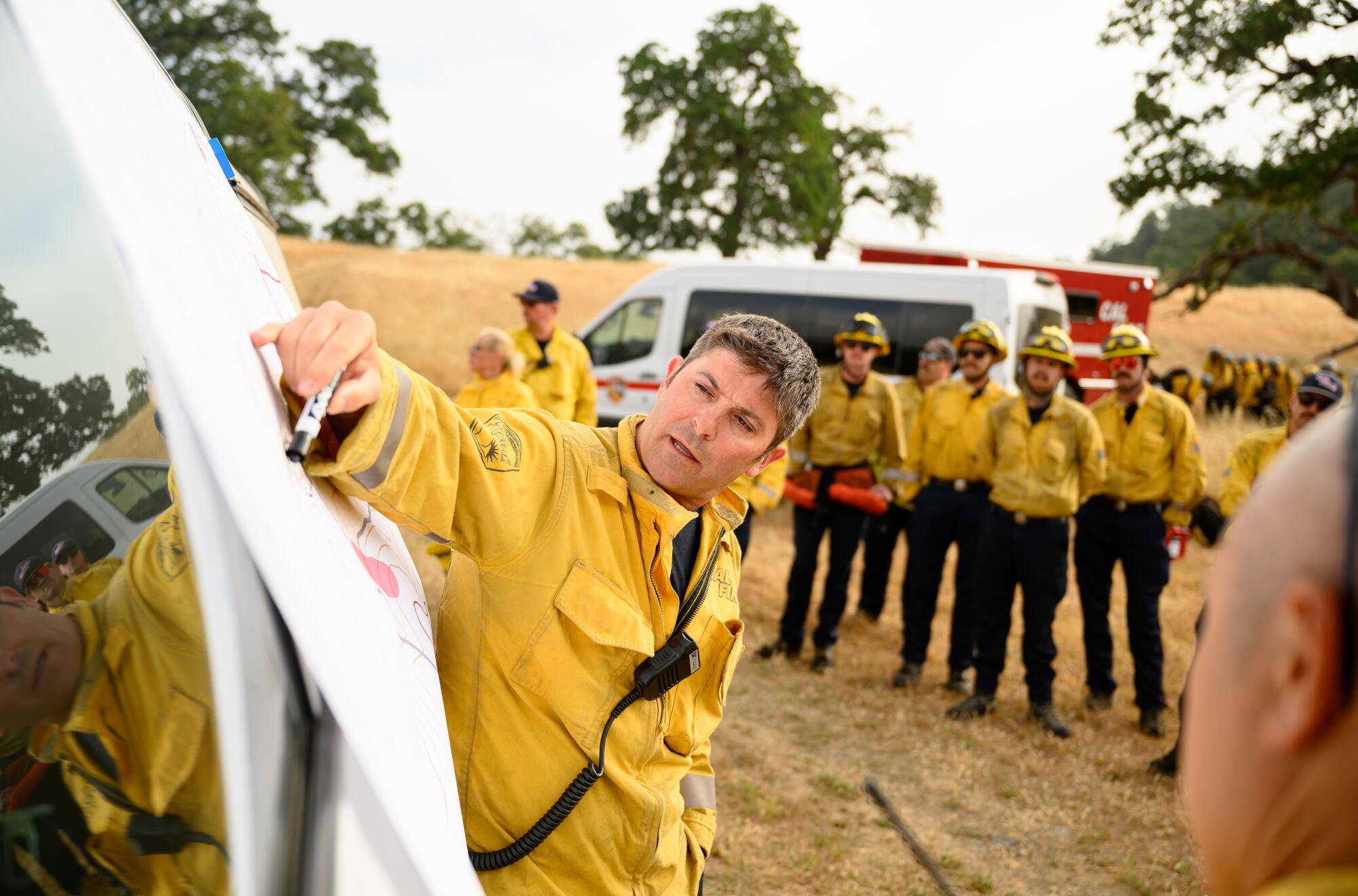 Un pompier dans une veste jaune utilise un marqueur et une carte pour tracer une brûlure prescrite.