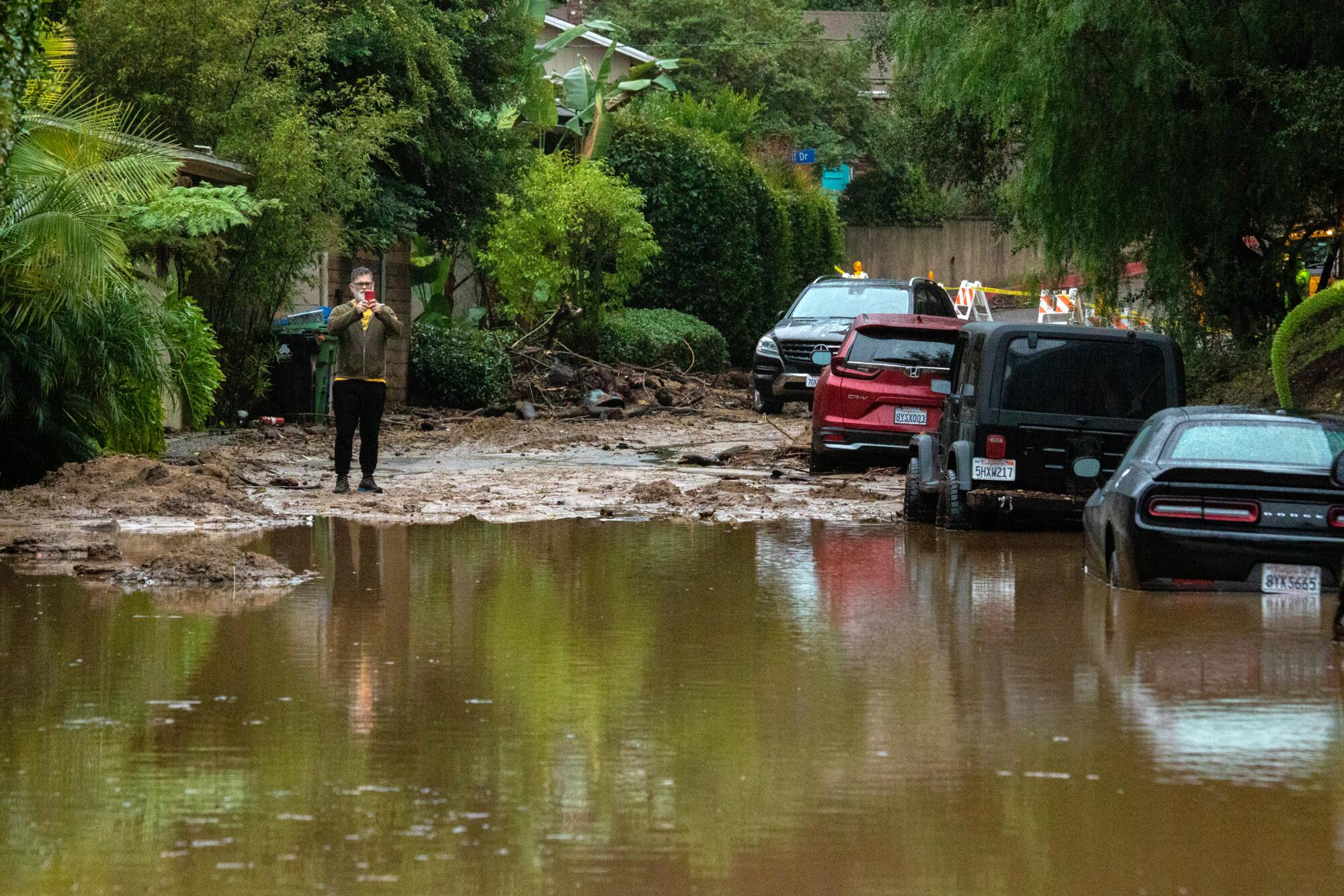 Un résident jette un coup d'œil à Mudslide et a inondé la fermeture de la rue à Studio City en 2023.
