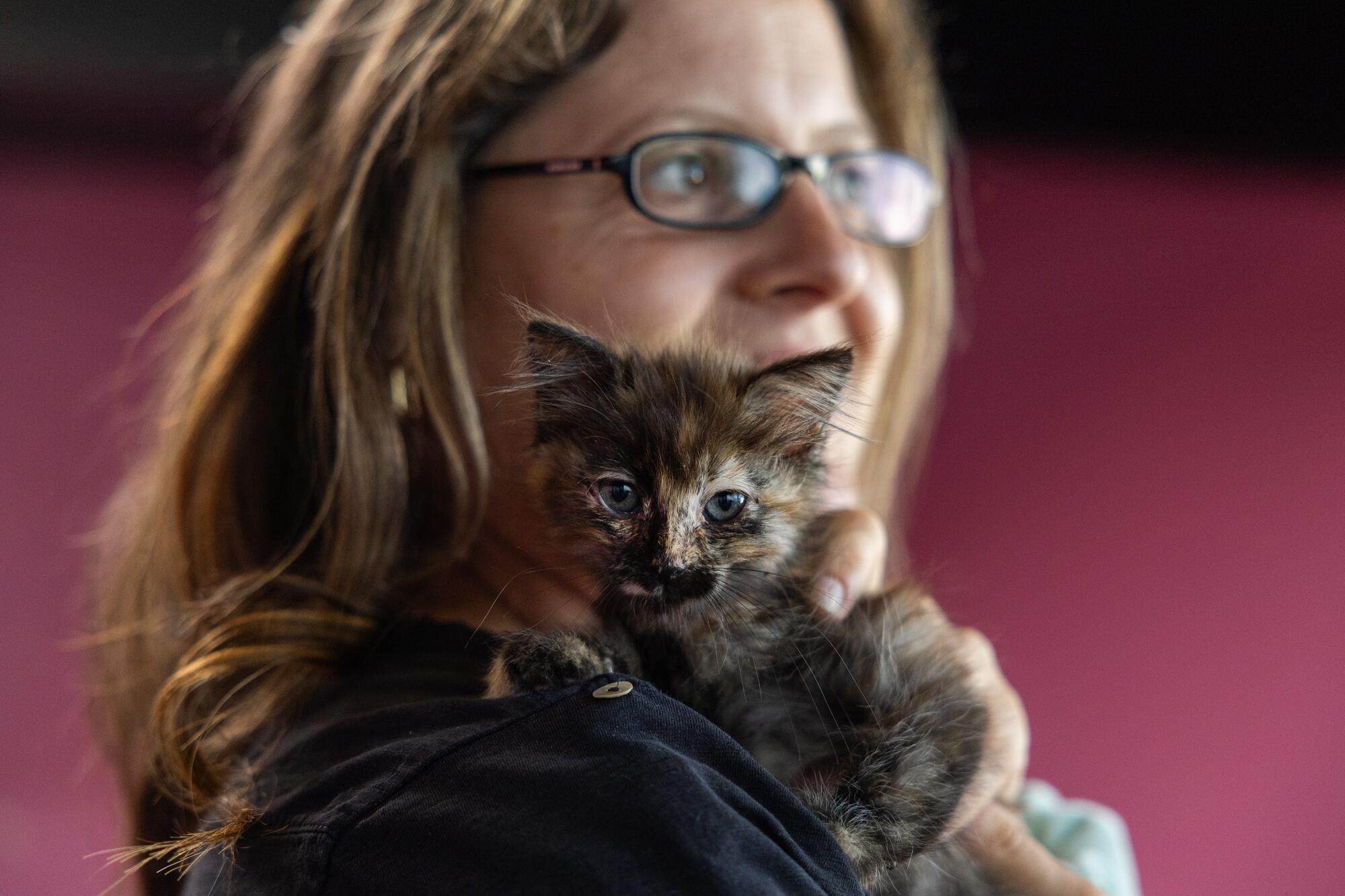 Une femme tient un chaton sur son épaule.
