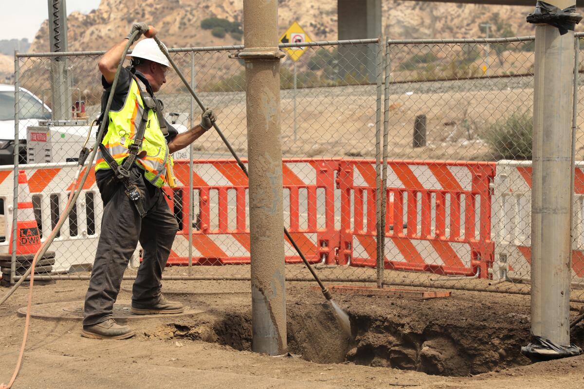 Un travailleur dans un hardhat et un gilet réfléchissant abaisse un outil dans un trou.