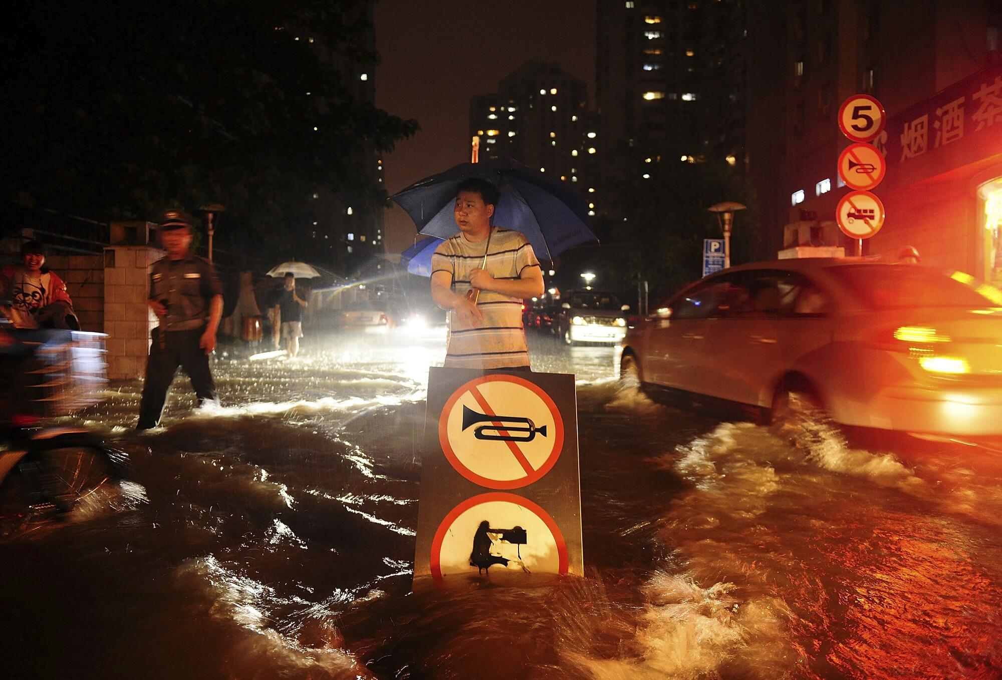 Un homme utilise un panneau pour signaler les automobilistes traversant une rue inondée en Chine. 
