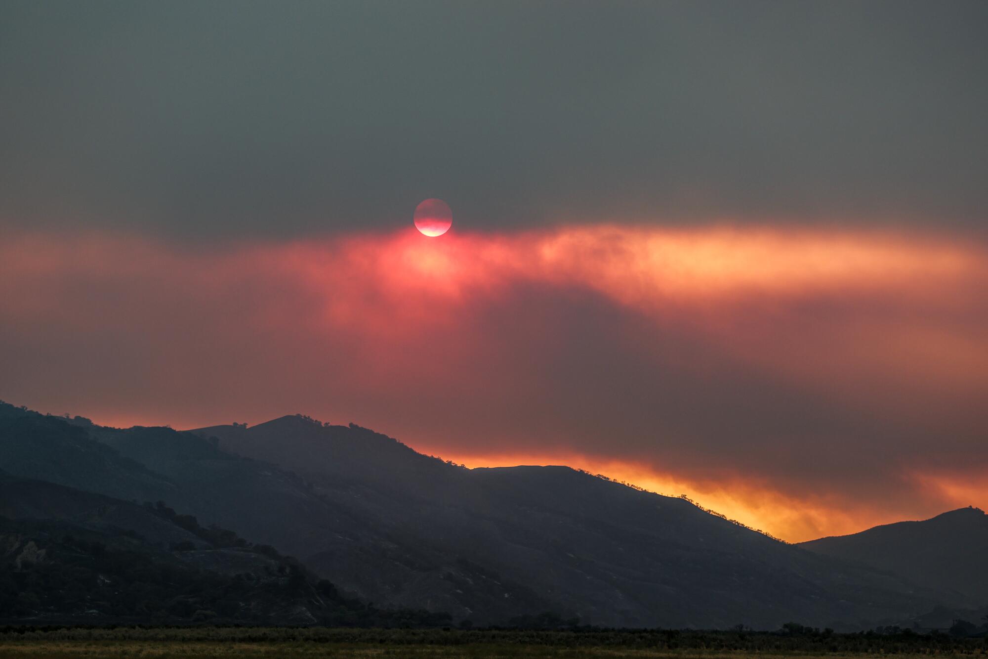 La fumée d'un feu filtre la lumière du soleil sur les collines
