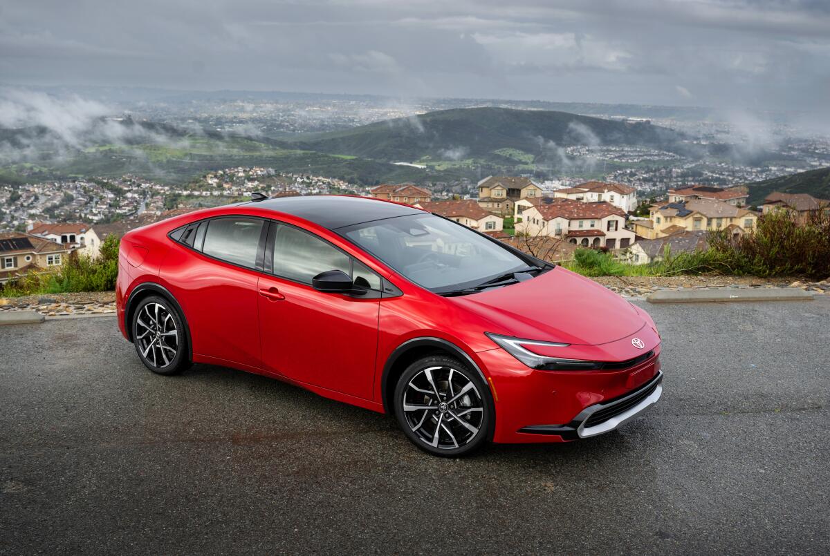 Une voiture rouge vif garée sur une route surplombant les maisons et les collines