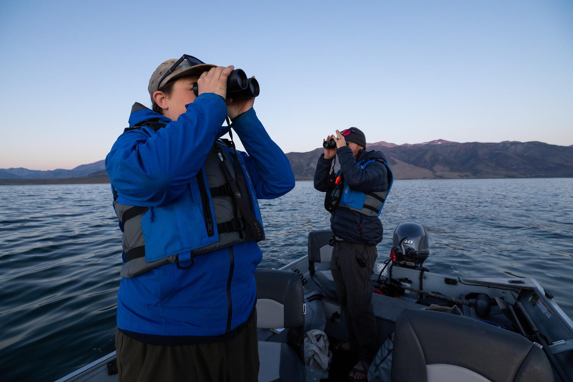 Deux personnes debout dans un bateau, regardant à travers des jumelles, sur un lac