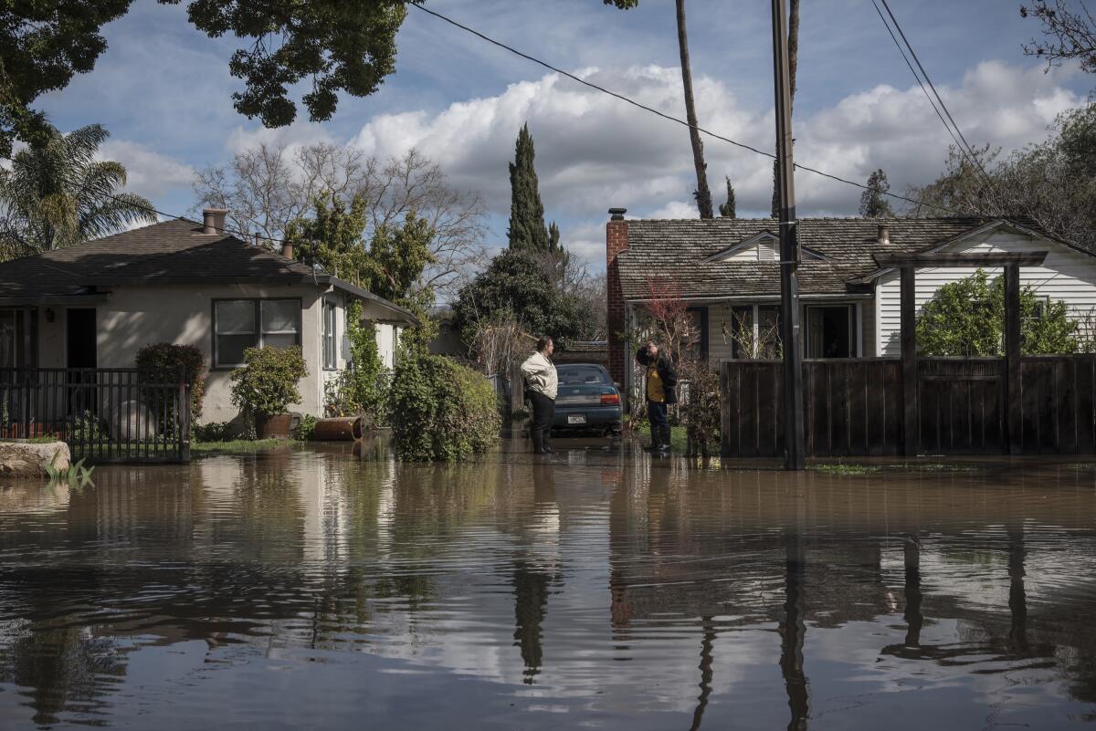 Des voisins discutent au milieu des eaux de crue dans un quartier résidentiel. 