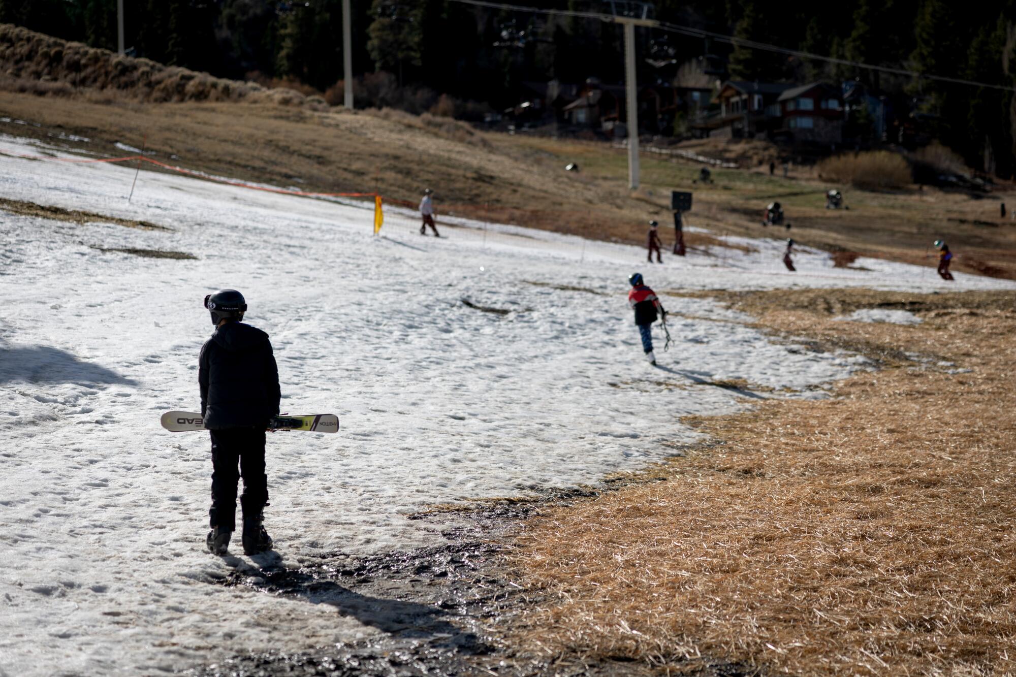 Les skieurs et planchistes parcourent les zones dénudées à côté du sol enneigé du Big Bear Mountain Resort.