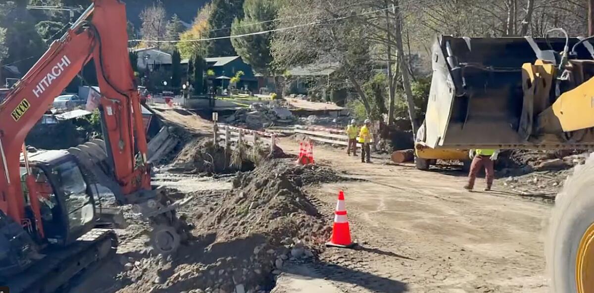 Des bulldozers et des gilets jaunes se tiennent à côté d’un pont en terre.