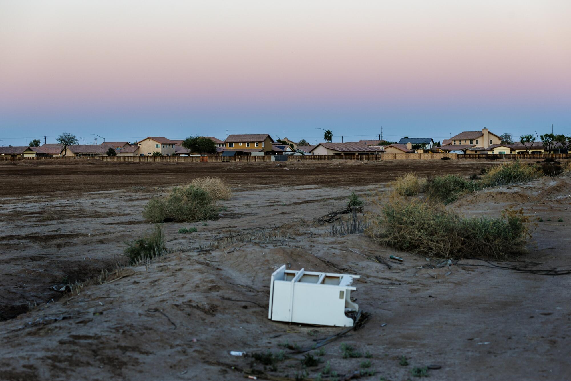 Une armoire repose sur le côté dans la terre sur un terrain découvert avec des maisons et le ciel en arrière-plan.