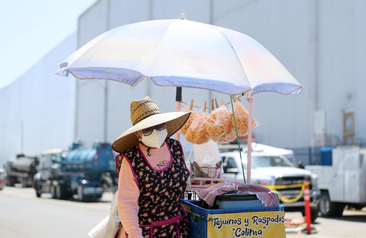 Un vendeur ambulant coiffé d’un chapeau de paille pousse un chariot de nourriture avec un parapluie. 
