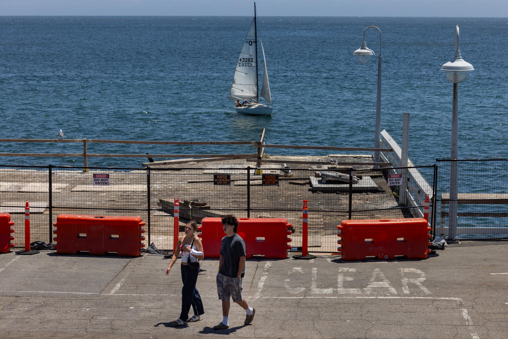 les gens passent devant une jetée et un voilier