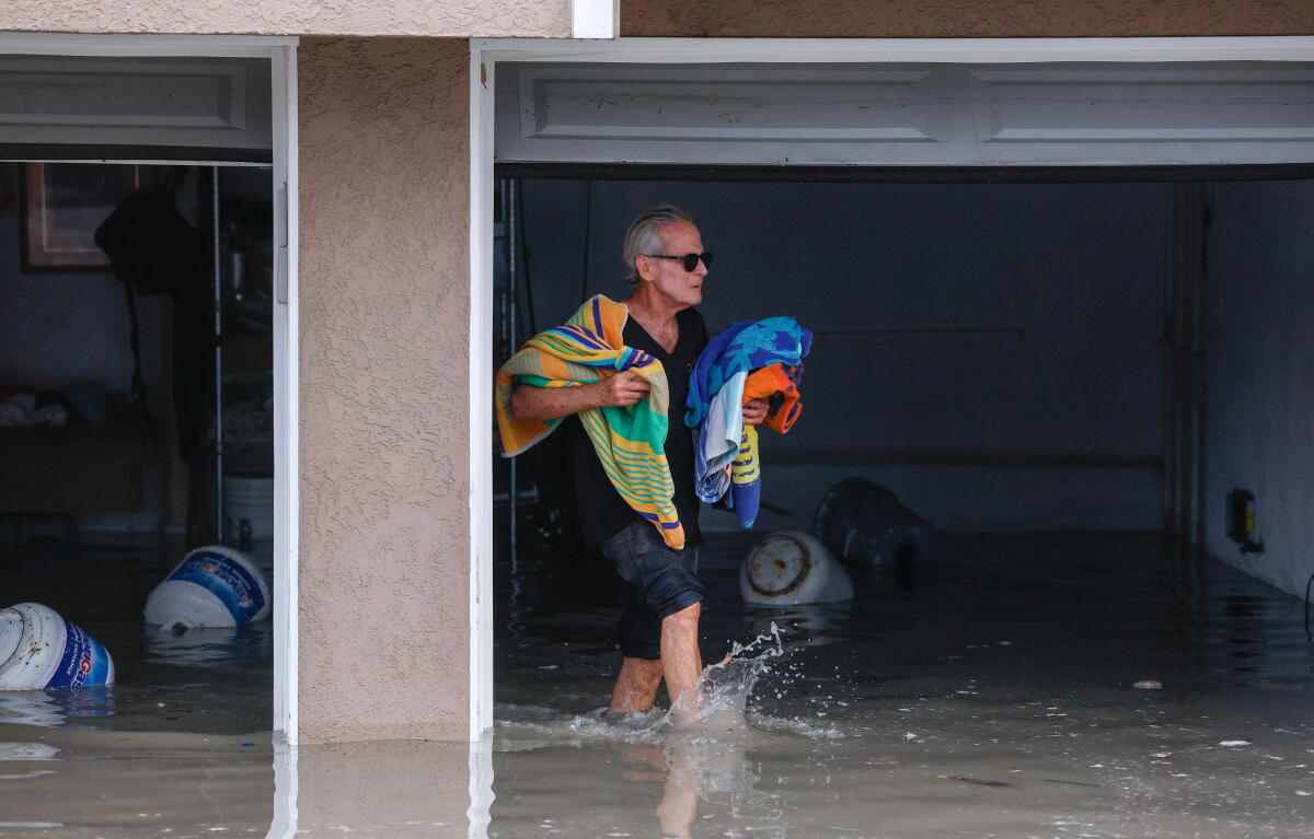 Un homme sort des serviettes de plage d’un garage inondé.