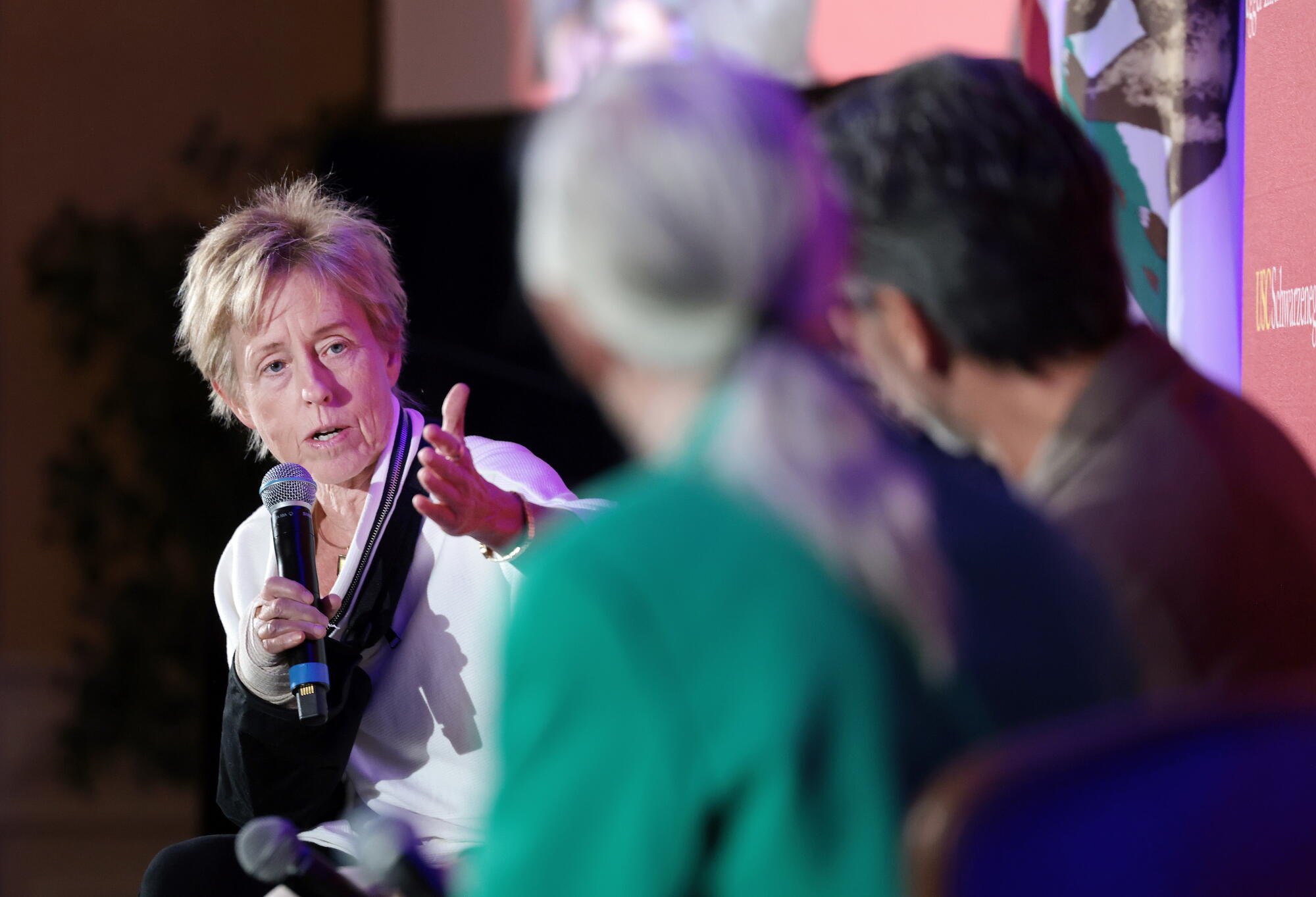 Une femme parle en tenant un microphone de la main droite et en tendant l’autre main.