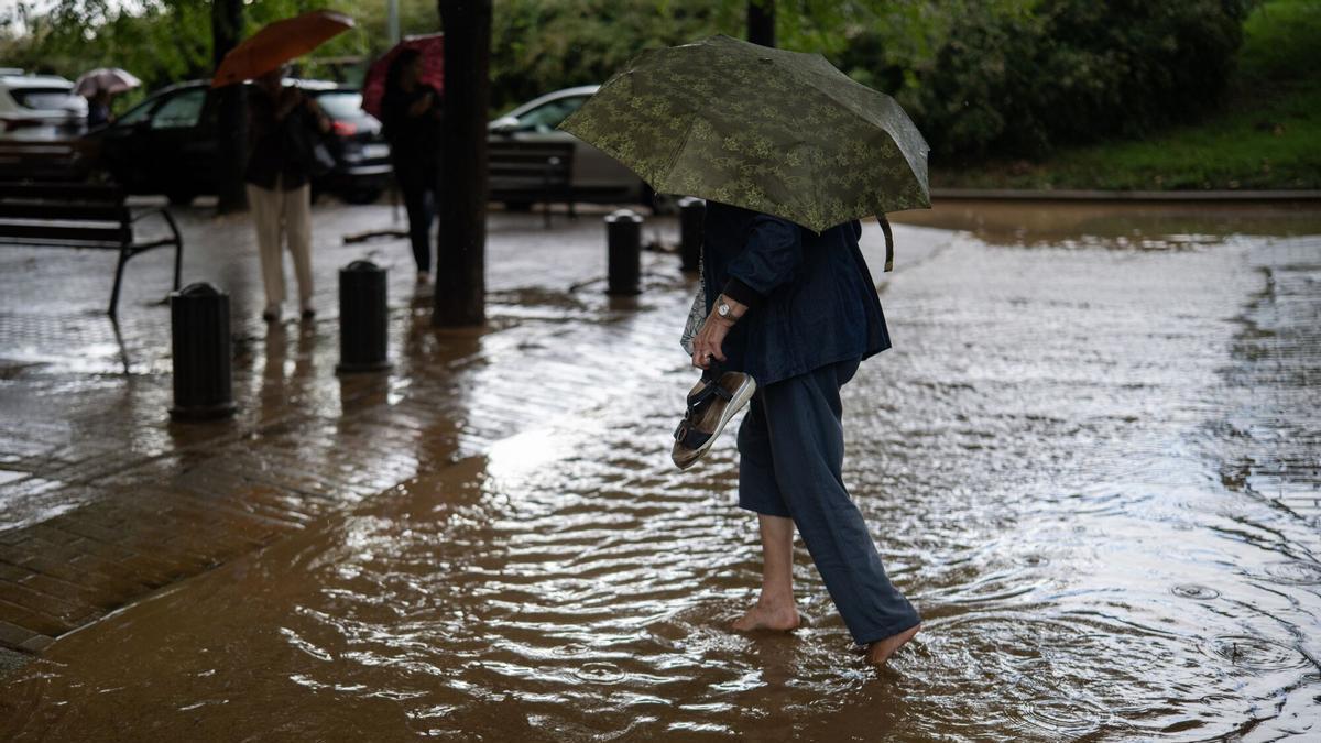 Una mujer cruza a través de la lluvia acumulada en la calle en el barrio de Canyelles-Nou Barris.